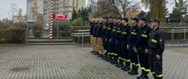Strażacy stoją na placu jednostki i przy maszcie z flagą odśpiewali hymn państwowy. 