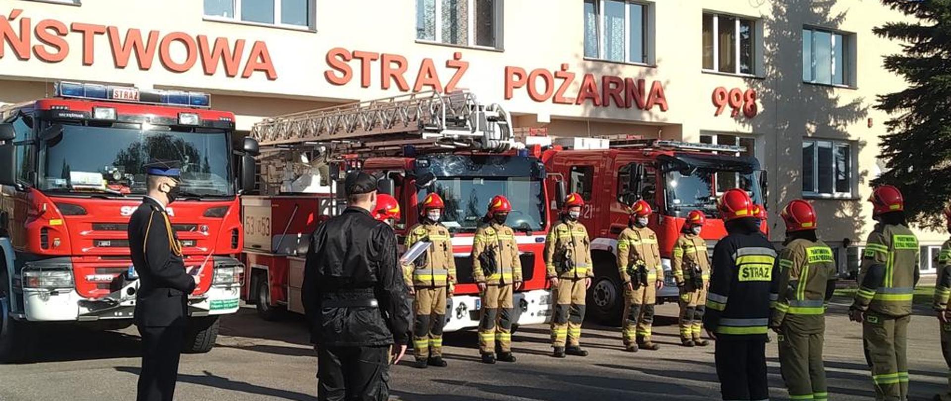 Strażacy podczas zmiany służby na tle budynku Państwowej Straży Pożarnej w Morągu.