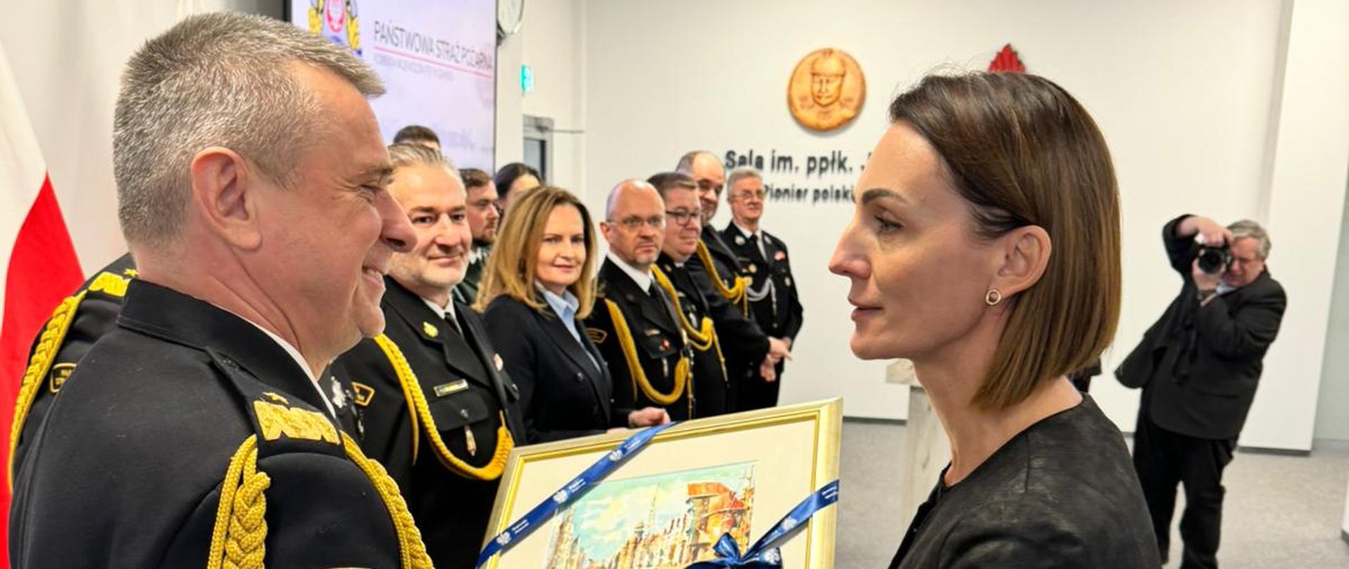 kobieta (wojewoda) wręcza i mężczyźnie (strażak) pamiątkową grafikę