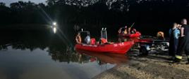 Zapadający zmrok łódź motorowa na tafli jeziora obok strażacy stojący na piasku
