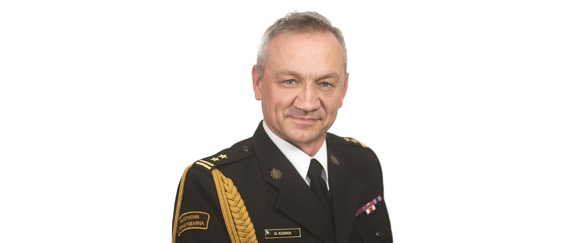 Zdjęcie portretowe na jasnym tle zastępcy komendanta powiatowego Państwowej Straży Pożarnej w Lublińcu brygadier Daniel Kozioł w mundurze galowym.