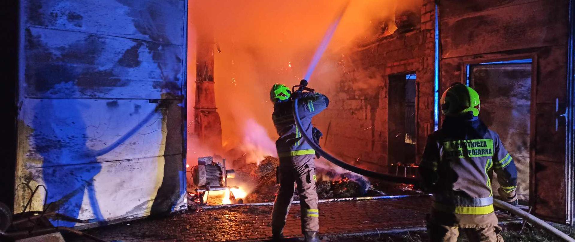 dwóch strażaków gasi pożar budynku