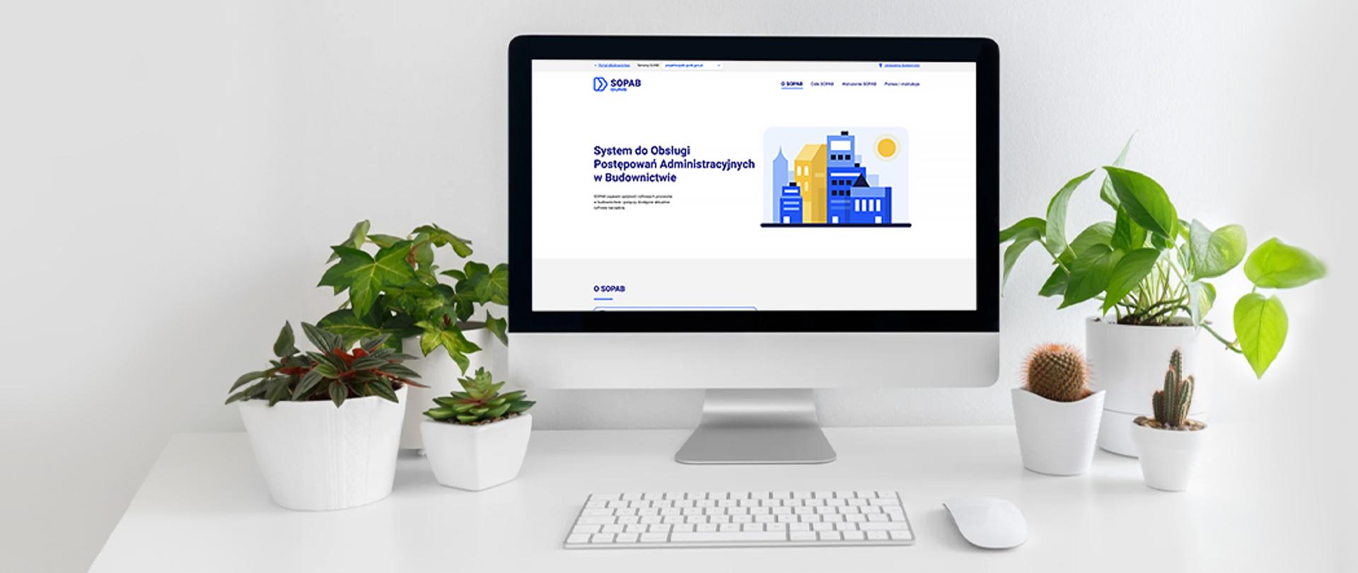 Na ekranie komputera widoczna jest strona internetowa Systemu do Obsługi Postępowań Administracyjnych w Budownictwie (SOPAB). Na biurku stoją rośliny w białych doniczkach, a obok znajduje się klawiatura i myszka komputerowa.