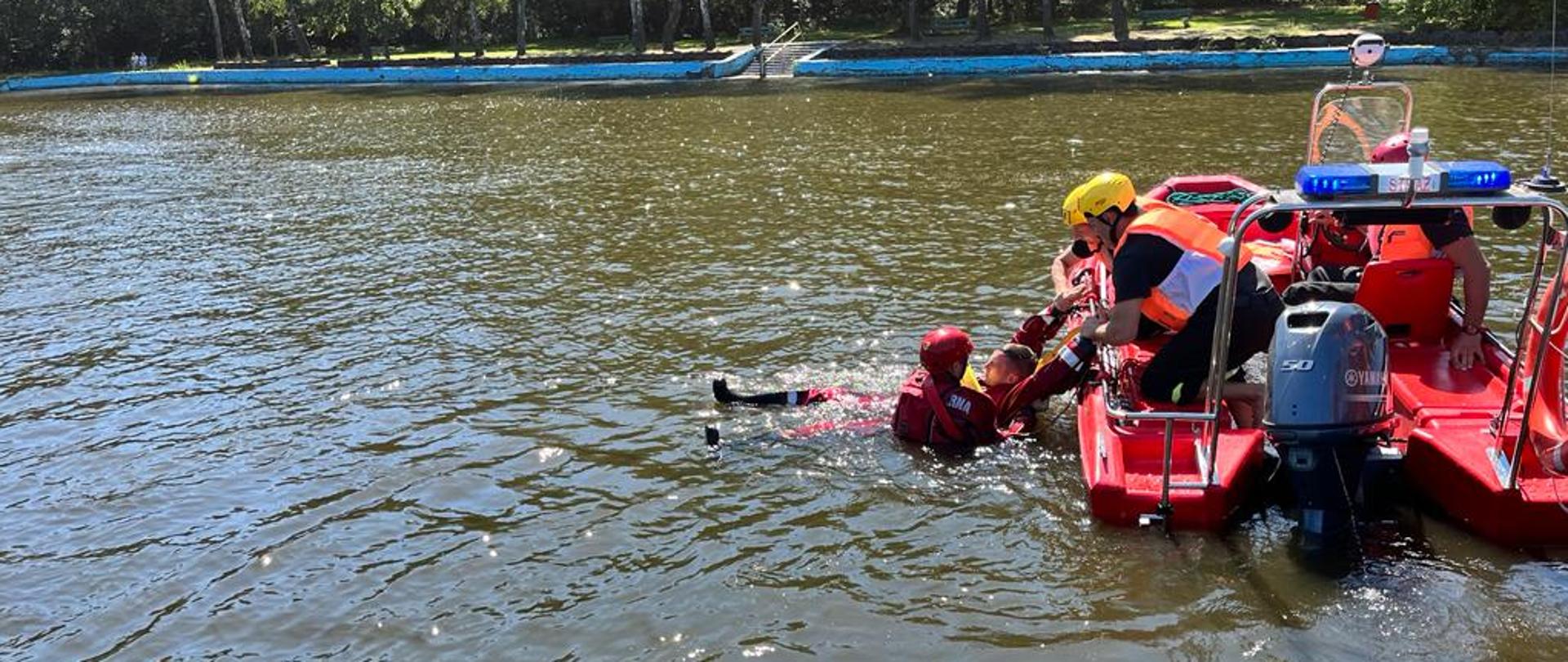 Strażacy podejmują poszkodowanego z wody na łódź ratowniczą. 
