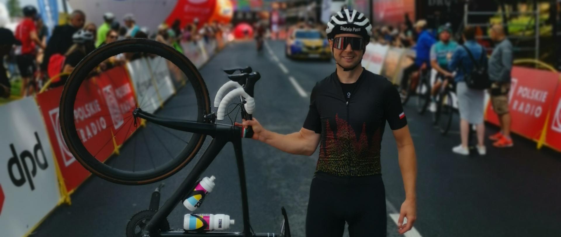 Reprezentant Komendy Powiatowej PSP w Proszowicach stoi na mecie zawodów trzymając rower