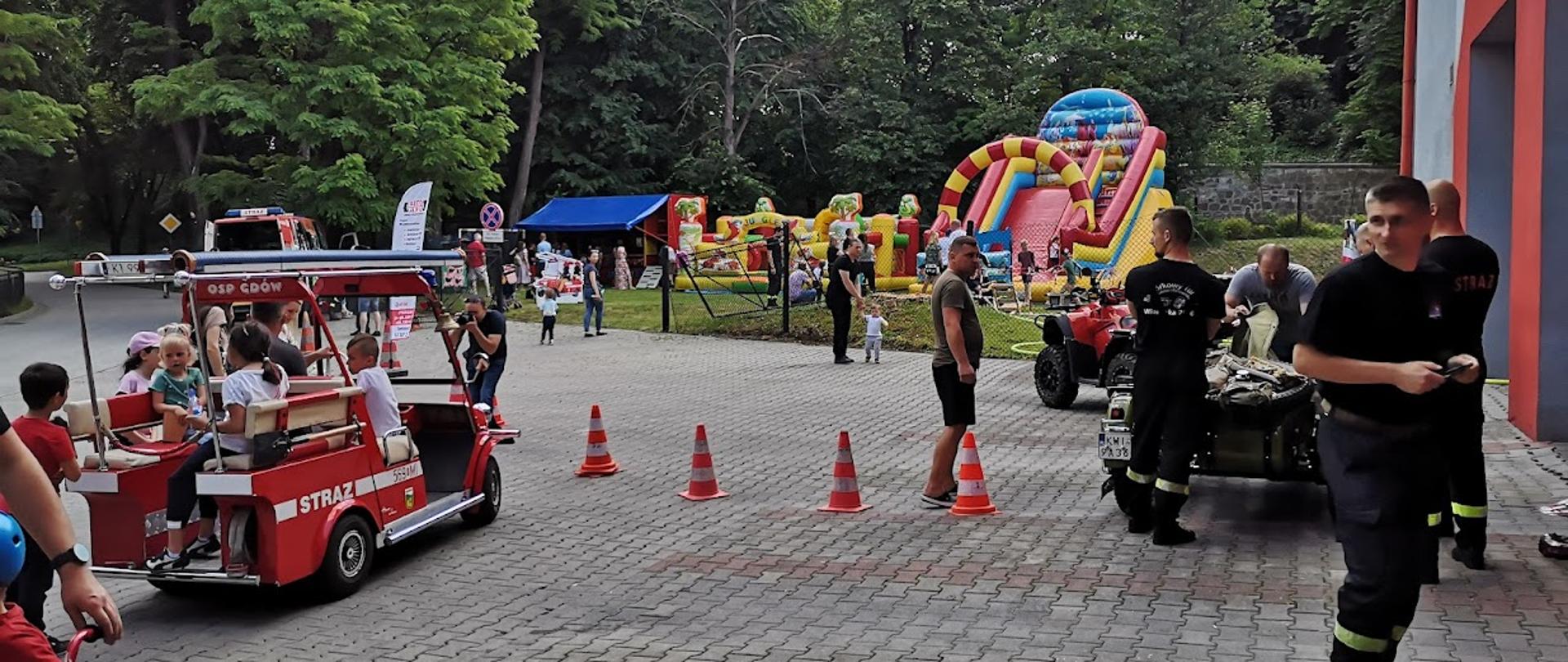 Na zdjęciu melex strażacki, który przewozi dzieci,w tle dmuchańce. Strażacy na placu.