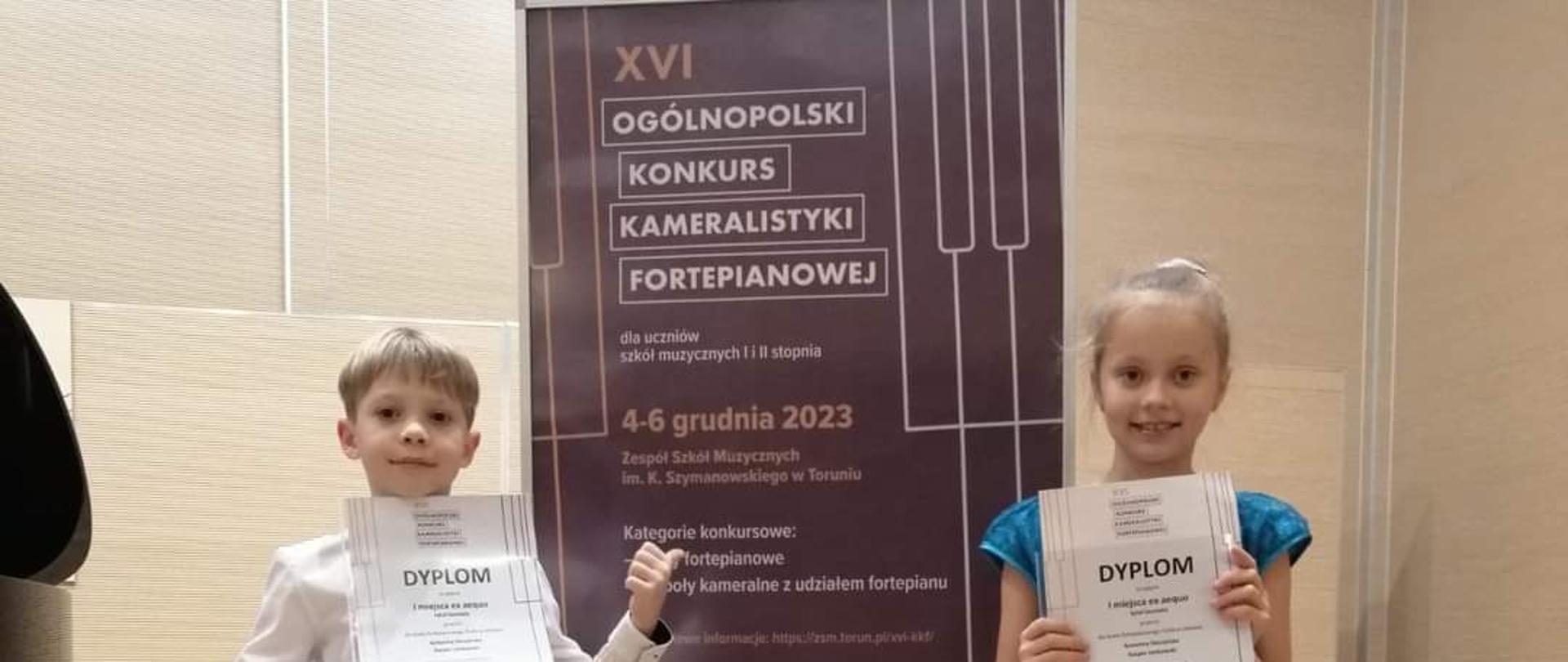 na zdjęciu przy tablicy informacyjnej dwoje uczniów z dyplomami gratulacyjnymi