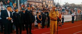 Widok z przodu. Przemawia Małopolski Komendant Wojewódzki. Z tyłu zaproszeni goście. W tle widownia. 