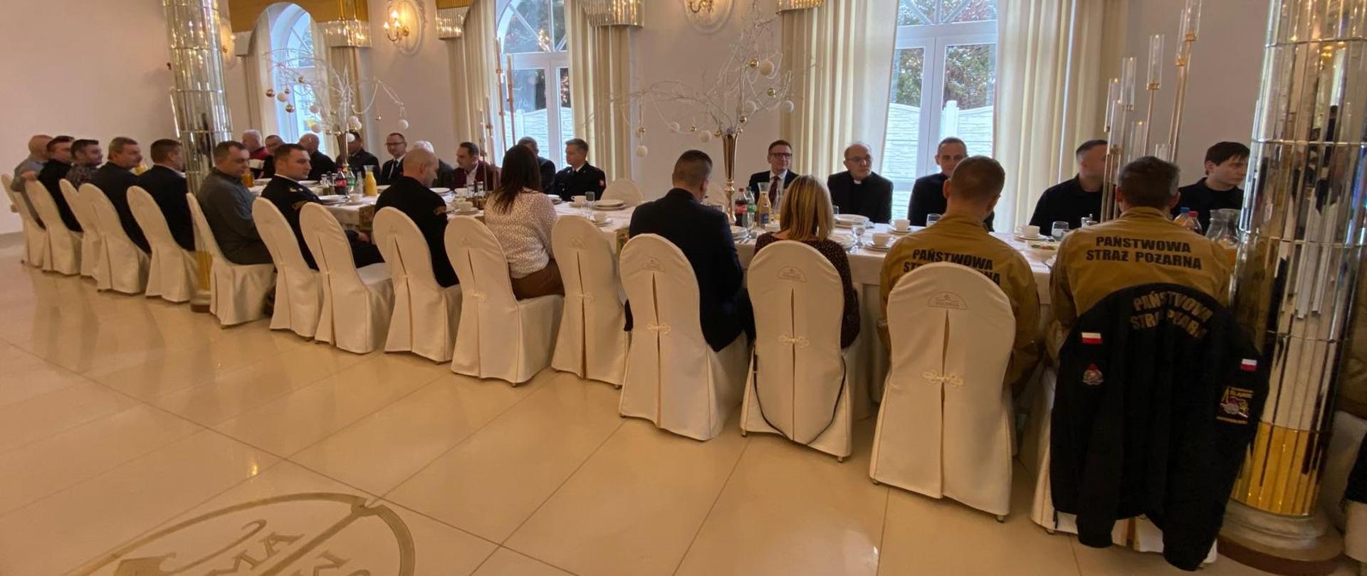 Widok na uczestników siedzących przy nakrytych stołach.