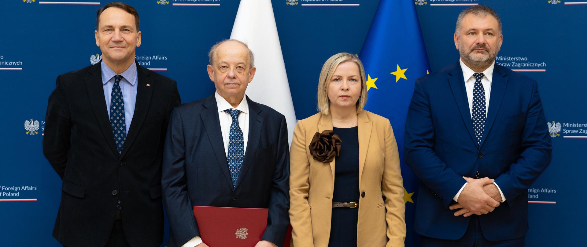 Cztery osoby stoją na tle ścianki z logotypem MSZ.