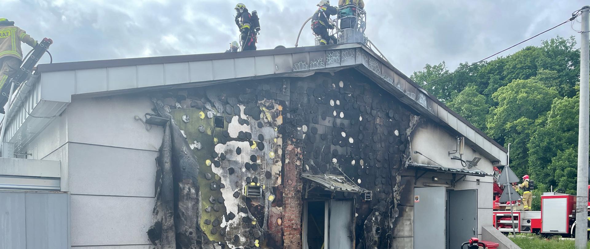 widok nadpalonej elewacji budynku dyskontu spożywczego, na dachu pracujący strażacy