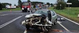 Rozbity pojazd, w tle wozy bojowe Państwowej Straży Pożarnej