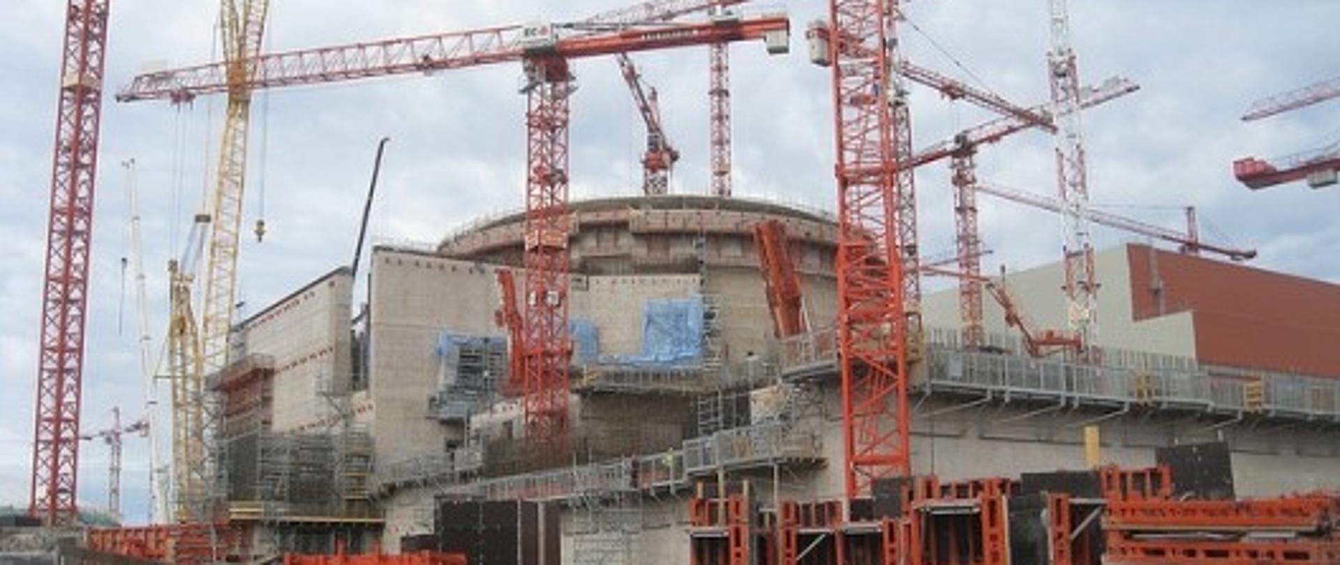 Zdjęcie przedstawiające elektrownię jądrową trzeciej generacji w budowie widać las dźwigów i betonową konstrukcję elektrowni