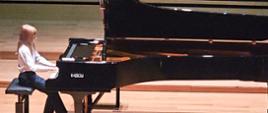 Chłopiec gra na fortepianie Fazioli na estradzie sali koncertowej - zbliżenie.