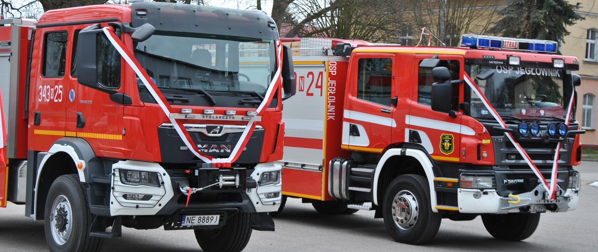 Dwa pojazdy ratowniczo gaśnicze widziane z przodu. w tle zabudowanie miejskie.