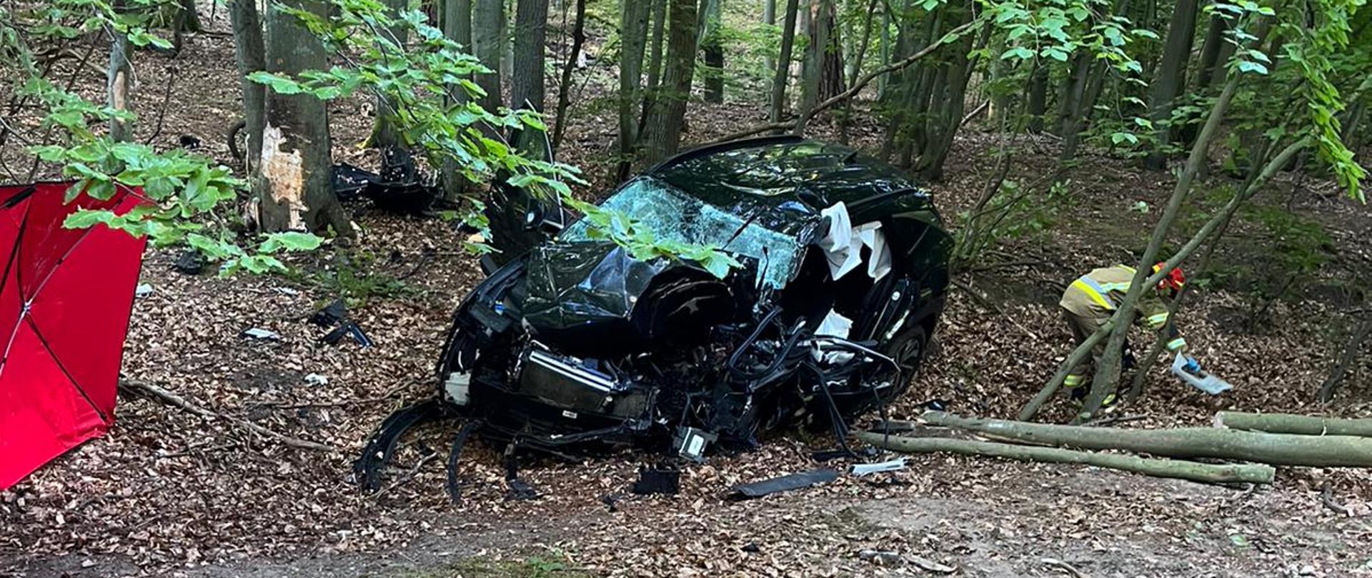 Rozbity pojazd w lesie przy drodze.