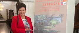 Na zdjęciu p. Dyrektor Dorota Kłodzińska przed plakatem promującym wystawę