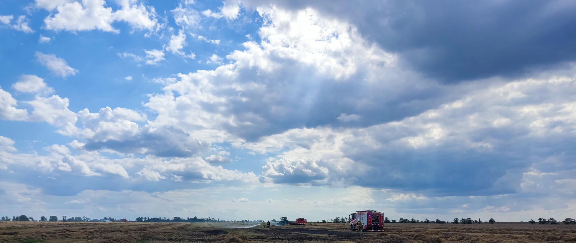 Strażacy na polu gaszą ściernisko i słomę po kombajnie.
