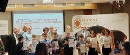 Zdjęcie kolorowe. Grupa osób stojących na scenie. Laureaci XVII Grudziądzkiego Konkursu Akordeonowego wraz z nauczycielami. Dzieci trzymają w ręku dyplomy.