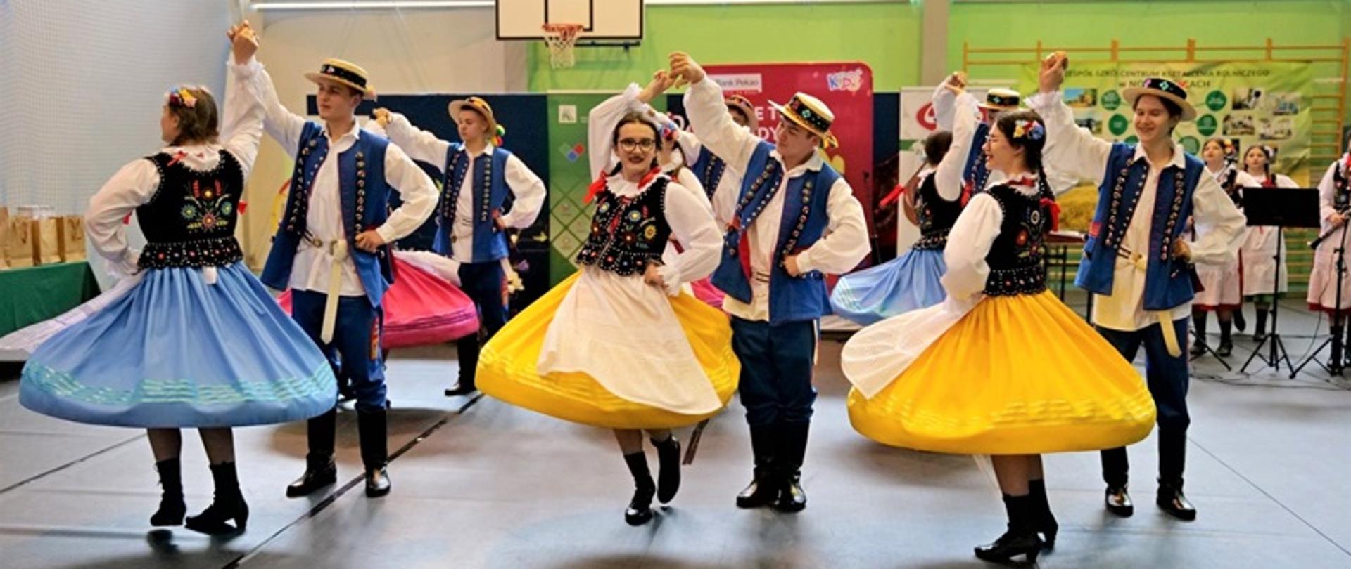 Prezentacja tańca w tradycyjnych strojach ludowych wykonywana przez uczniów szkolnego Zespołu Ludowego – ZCKR Nowosielce. Młodzi tancerze w kolorowych strojach tańczą w rytm muzyki