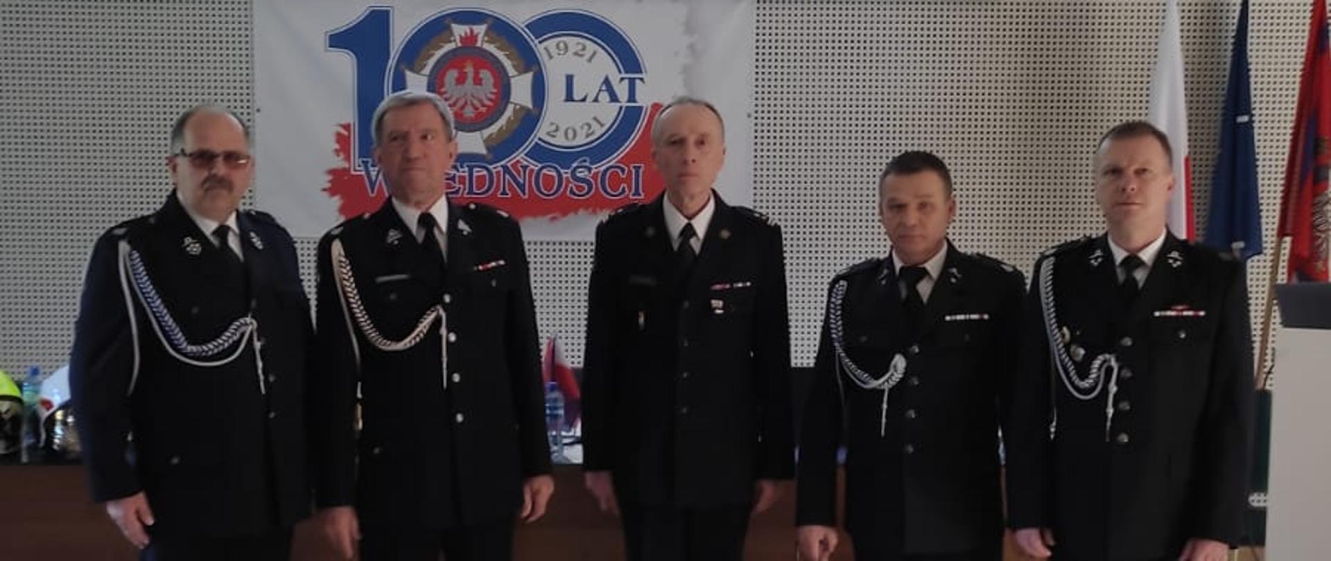 Zdjęcie przedstawia 5 mężczyzn podczas V Zjazd Oddziału Wojewódzkiego Ochotniczych Straży Pożarnych RP województwa zachodniopomorskiego. Znajdują się oni na sali.