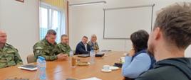 Spotkanie przedstawicieli służb podczas wizji terenowej. Uczestnicy rozmawiają siedząc za stołem konferencyjnym.