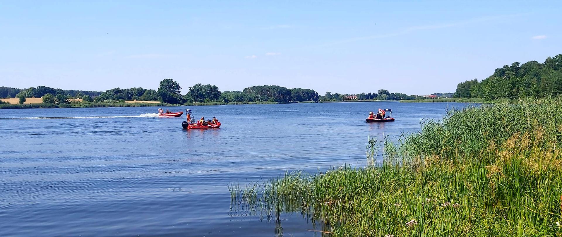 Widać trzy łodzie na jeziorze, na których pływają strażacy