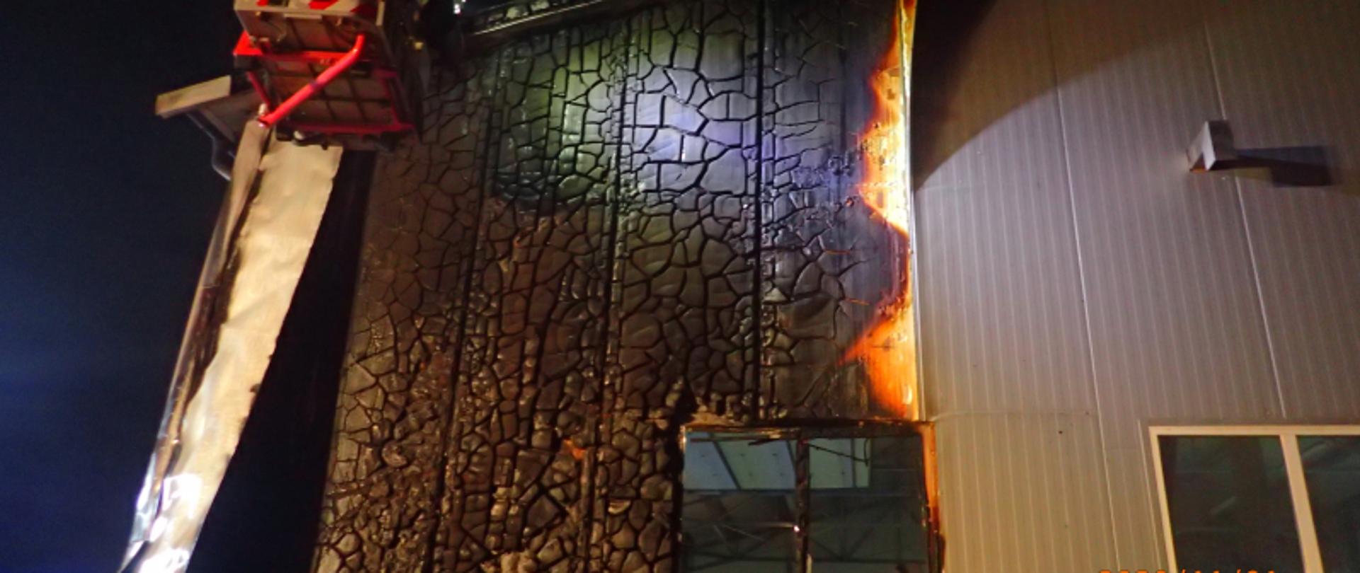 Widoczne uszkodzenia ściany szczytowej budynku oraz części poszycia dachowego, które uległo spaleniu. Budynek wykonany w technologii płyty warstwowej.