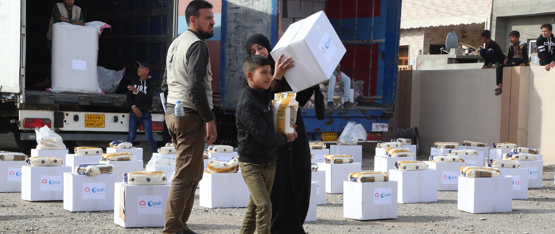 Boy and woman are carrying boxes given them by humanitarian organisation