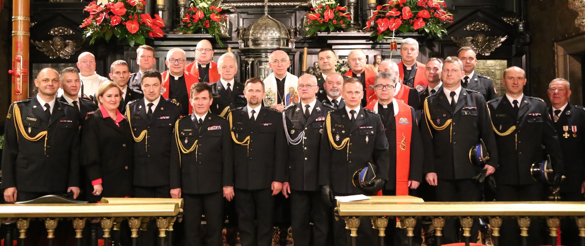 Grupowe zdjęcie uczestników uroczystej mszy (strażacy oraz duchowni) na tle obrazu NMP
