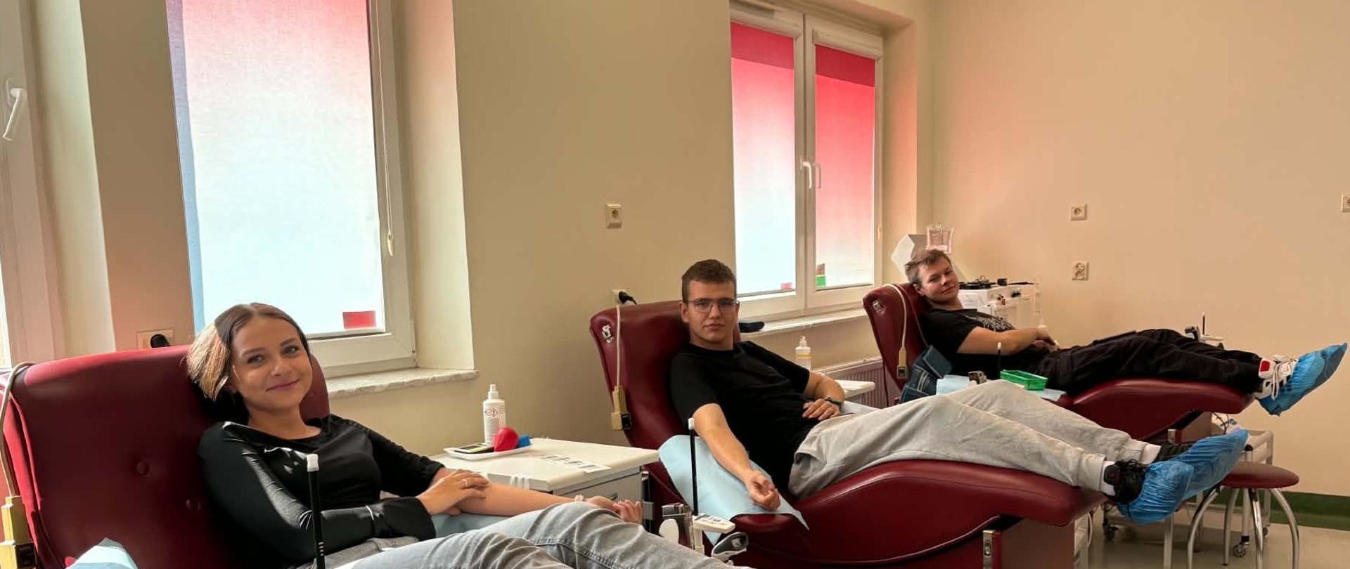 Trzy osoby leżą na fotelach medycznych podczas oddawania krwi w centrum krwiodawstwa.