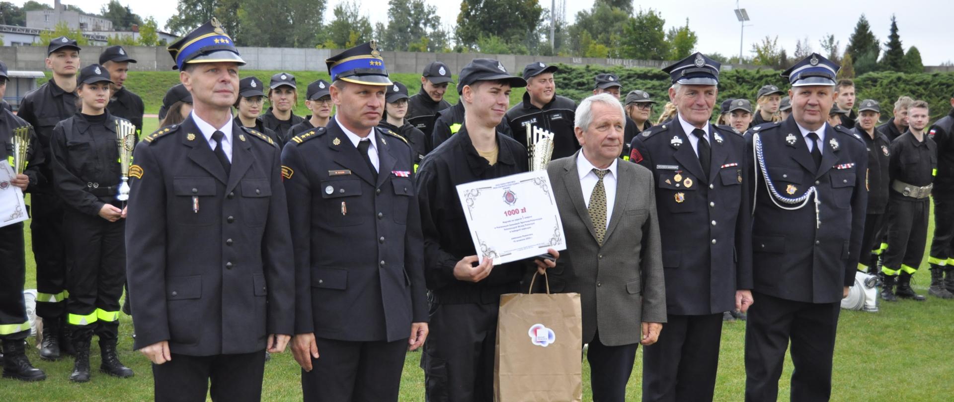 Zdjęcie przedstawia st. bryg. Marka Rusonia - Zastępcę Kujawsko-Pomorskiego Komendanta Wojewódzkiego PSP, Zbigniewa Sosnowskiego - Prezesa zarządu oddziału powiatowego Związku Ochotniczych Straży Pożarnych Rzeczypospolitej Polskiej w Brodnicy, st.bryg Andrzeja Góreckiego - Komendanta Powiatowego PSP w Brodnicy, przedstawicieli gminy, podczas pamiątkowego zdjęcia z przedstawicielem drużyny OSP Nieżywięć.