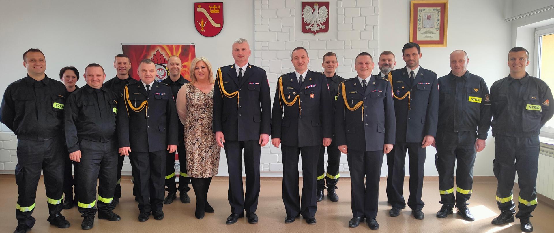 Pracownicy Komendy Powiatowej PSP w Proszowicach stoją w grupie, w tle godło państwowe