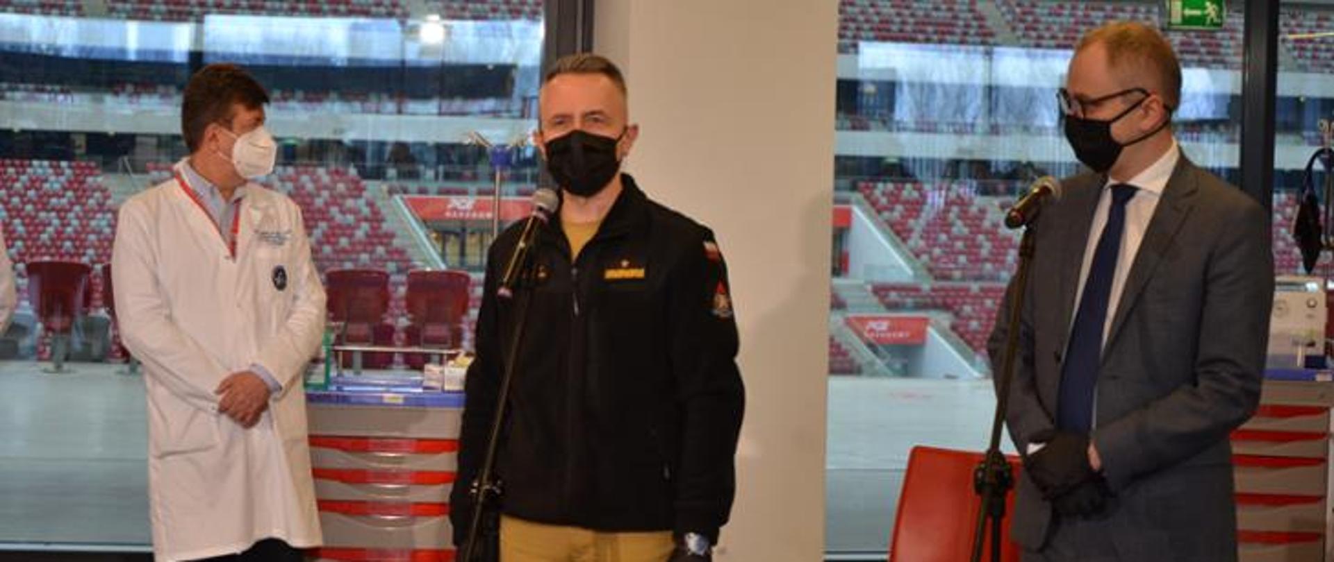 na zdjęciu widoczny Komendant Główny PSP przemawiający do mikrofonu na stadionie narodowym. Ubrany w nowy mundur służbowy strażaka PSP. 