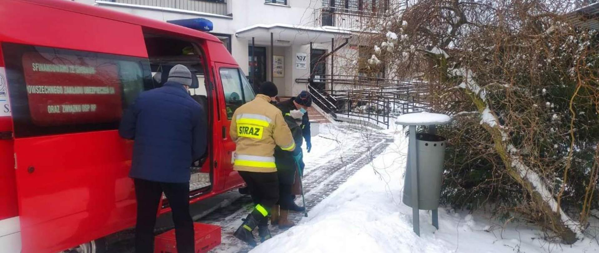 Strażacy na tle samochodu pomagają starszej kobiecie 