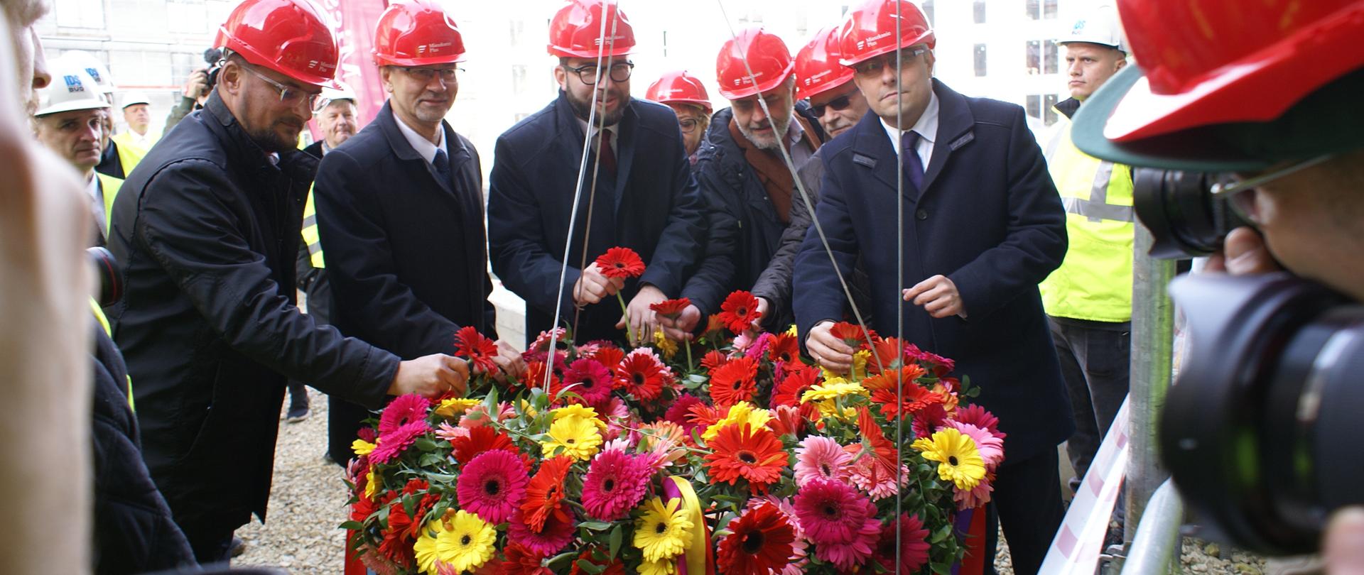 uczestnicy uroczystości umieszczają kwiaty w wiesze, która zostanie wciągnięta w najwyższy punkt budynku