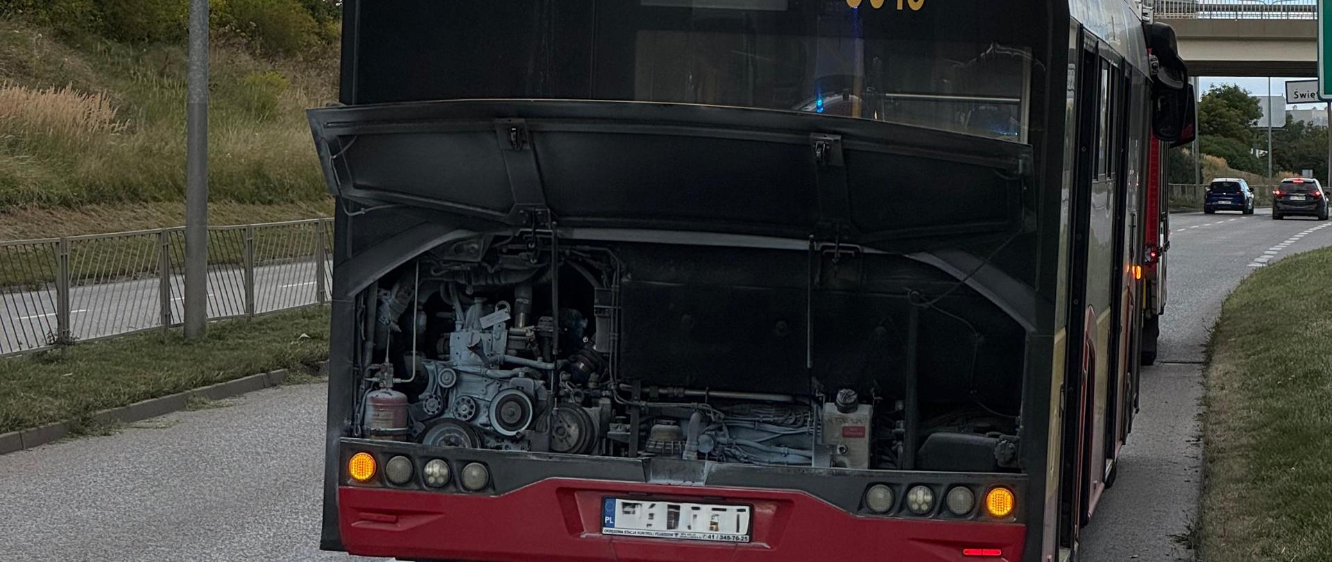 Zdjęcie przedstawia stojący na pasie jezdni autobus z otwartą klapą silnika. 