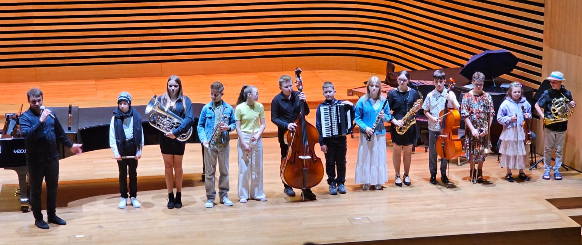 Na scenie stoi mężczyzna i dzieci ze swoimi instrumentami.