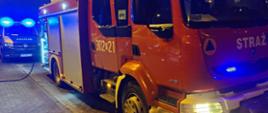 Na pierwszym planie pojazd pożarniczy a w tle pojazd Policji Pojazdy mają włączone niebieskie światła błyskowe