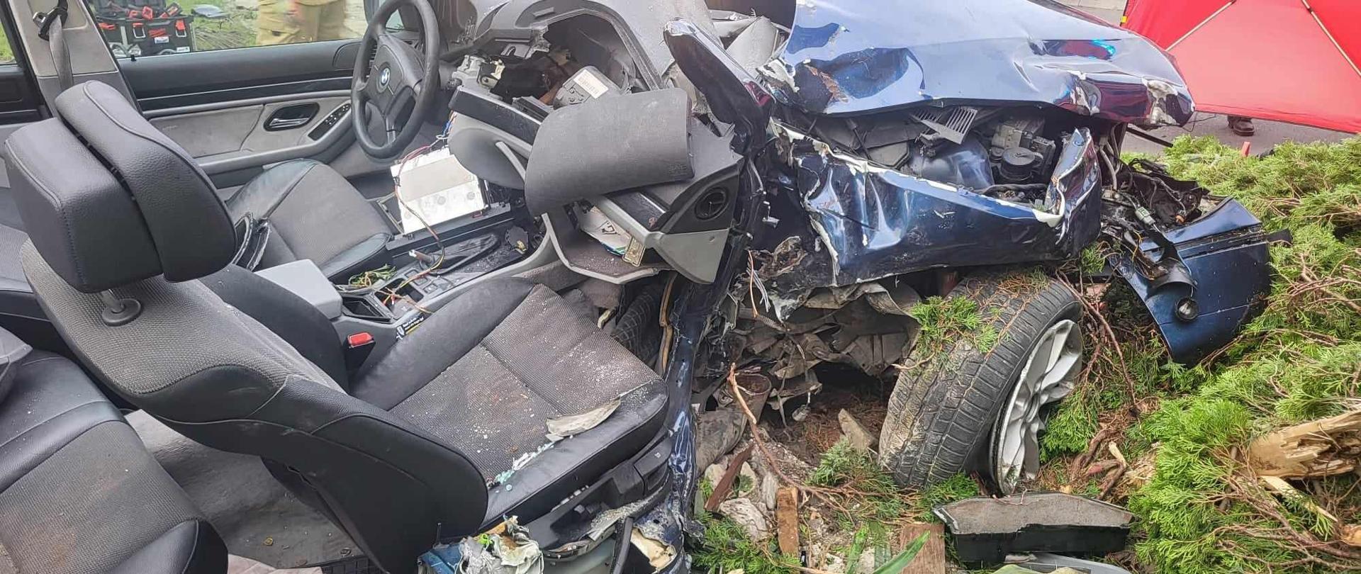 Na terenie z jednej posesji stoi samochód osobowy uczestniczący w wypadku. Pojazd jest koloru granatowego. Jest bardzo mocno uszkodzony, w tym ma odcięty dach. 