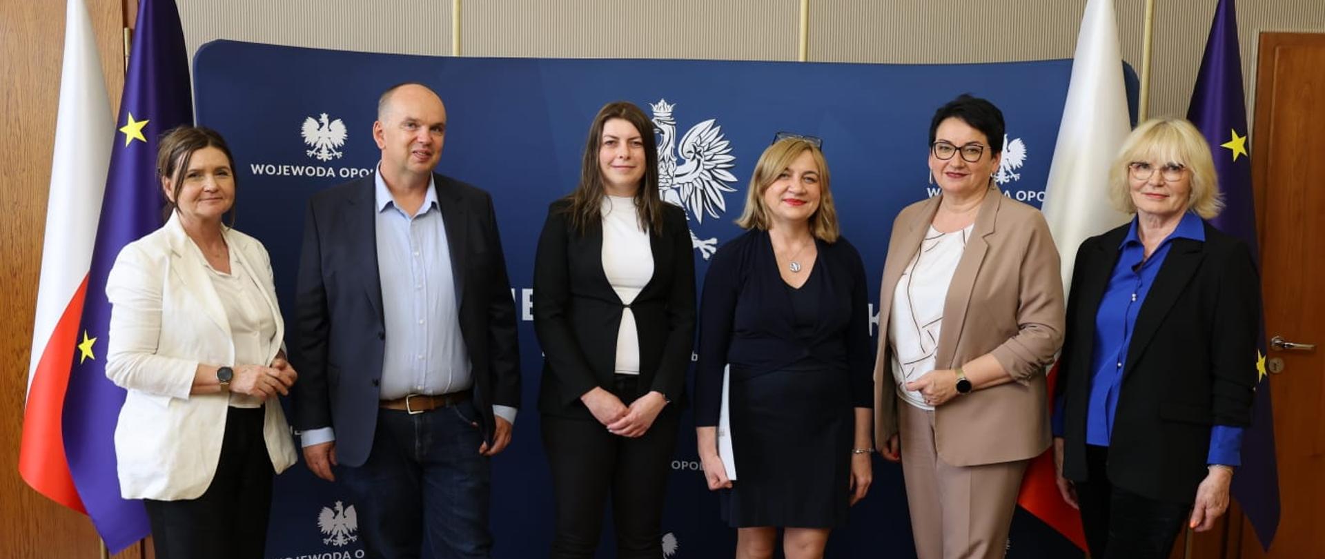 Uroczystość powołania konsultantów wojewódzkich w Sali Złotej Opolskiego Urzędu Wojewódzkiego. Na zdjęciu od lewej Zastępca Dyrektora Wydziału Zdrowia Beata Jabłońska, dr n. med. Jacek Hobot, Pani Katarzyna Bojkowska-Otrębska, dr hab. n. med. Beata Łabuz- Roszak, Wojewoda Opolski Monika Jurek oraz Dyrektor Wydziału Zdrowia Mirosława Kwatek-Hoffmann. Wszyscy stoją na tle granatowego baneru z napisem Wojewoda Opolski. Po lewej oraz prawej stronie widać flagi Polski oraz Unii Europejskiej. 