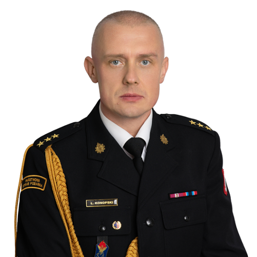 Zdjęcie przedstawia Łukasz Konopskiego, Zastępcę Komendanta Powiatowego Państwowej Straży Pożarnej w Zwoleniu. Jest to portret mężczyzny w mundurze galowym strażaka, z widocznymi dystynkcjami na pagonach. Na piersi munduru widoczne są baretki odznaczeń