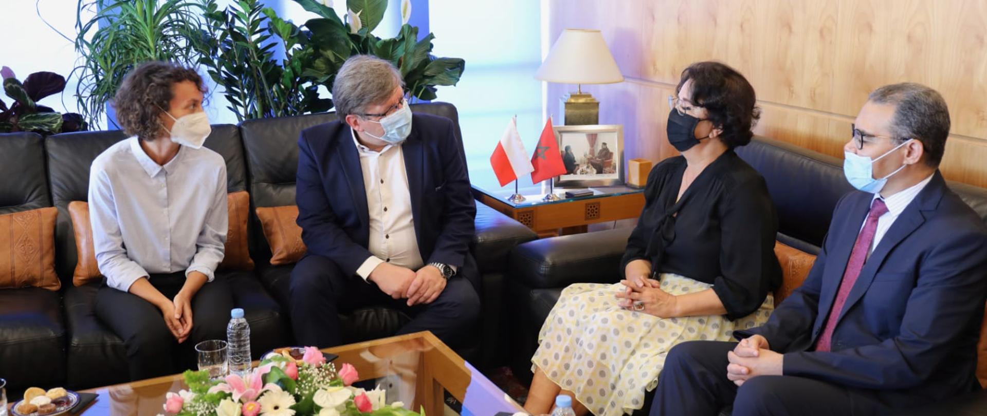 Zdjęcie w poziomie. Ludzie siedzą na kanapach wokół niskiego stołu.