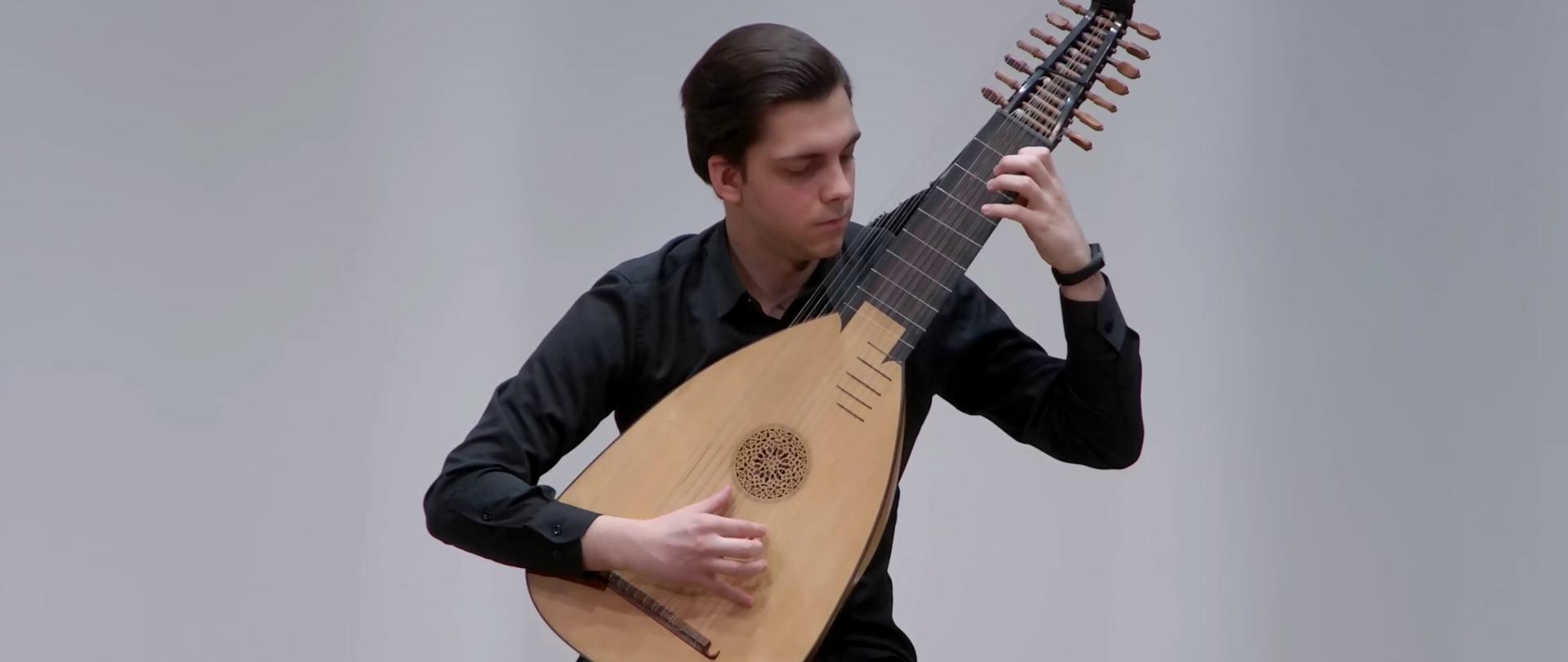 Zdjęcie - na estradzie podczas koncertu występuje młody instrumentalista, który gra na lutni.