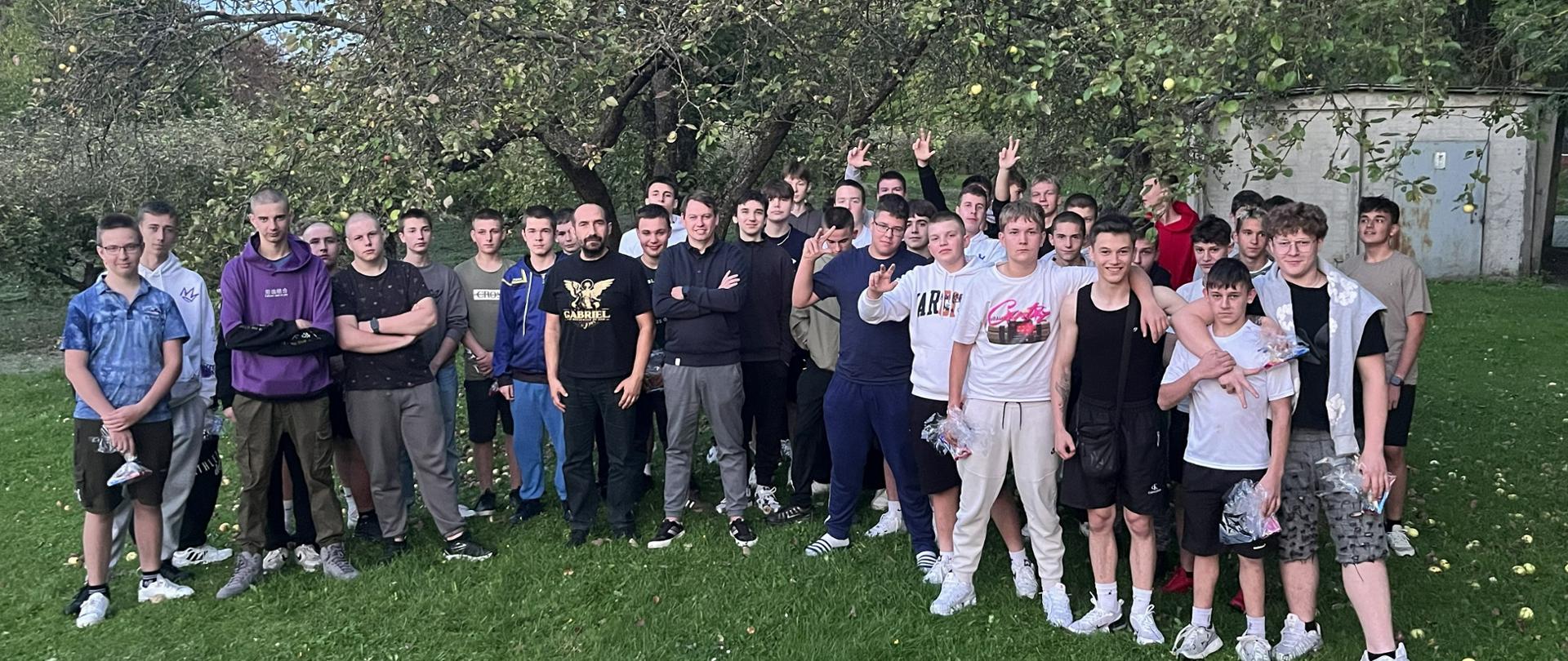 Grupa uczniów podczas wspólnego spotkania na świeżym powietrzu w sadzie.