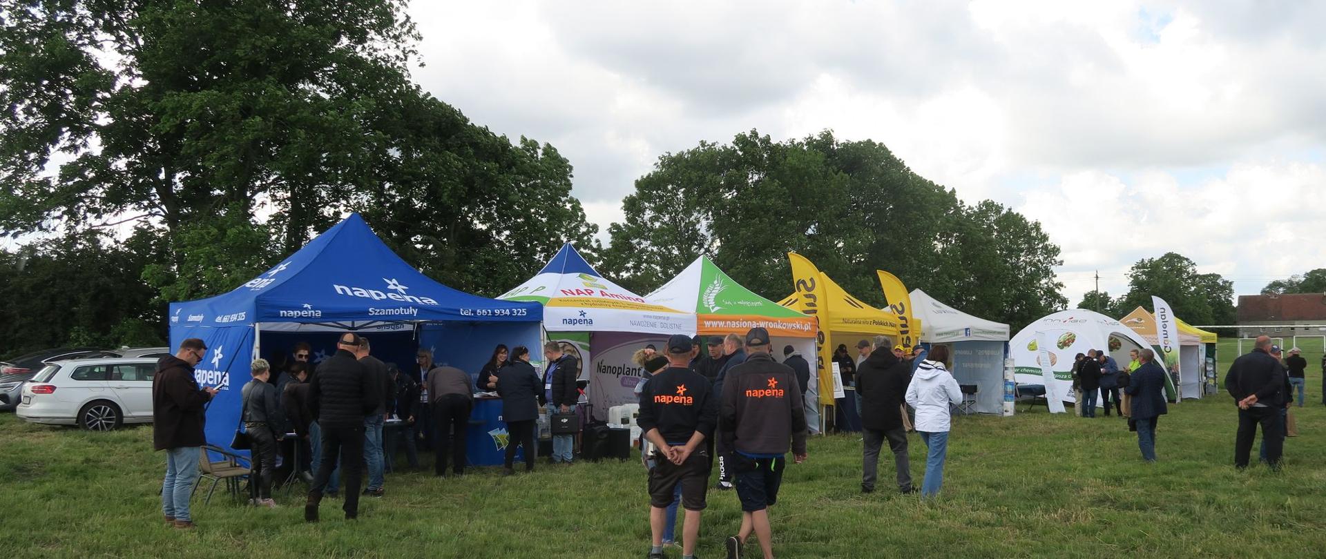Grupa ludzi na tle namiotów z ekspozycjami uczestników wydarzenia