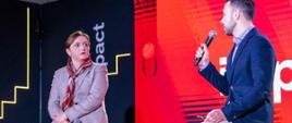 Wiceminister rozwoju i technologii Olga Semeniuk podczas dyskusji panelowej na Impact'22, minister siedzi na wysokim krześle, obok niej po prawej stronie siedzi dziennikarz prowadzący rozmowę, za ich plecami czerwony baner z napisem Impact