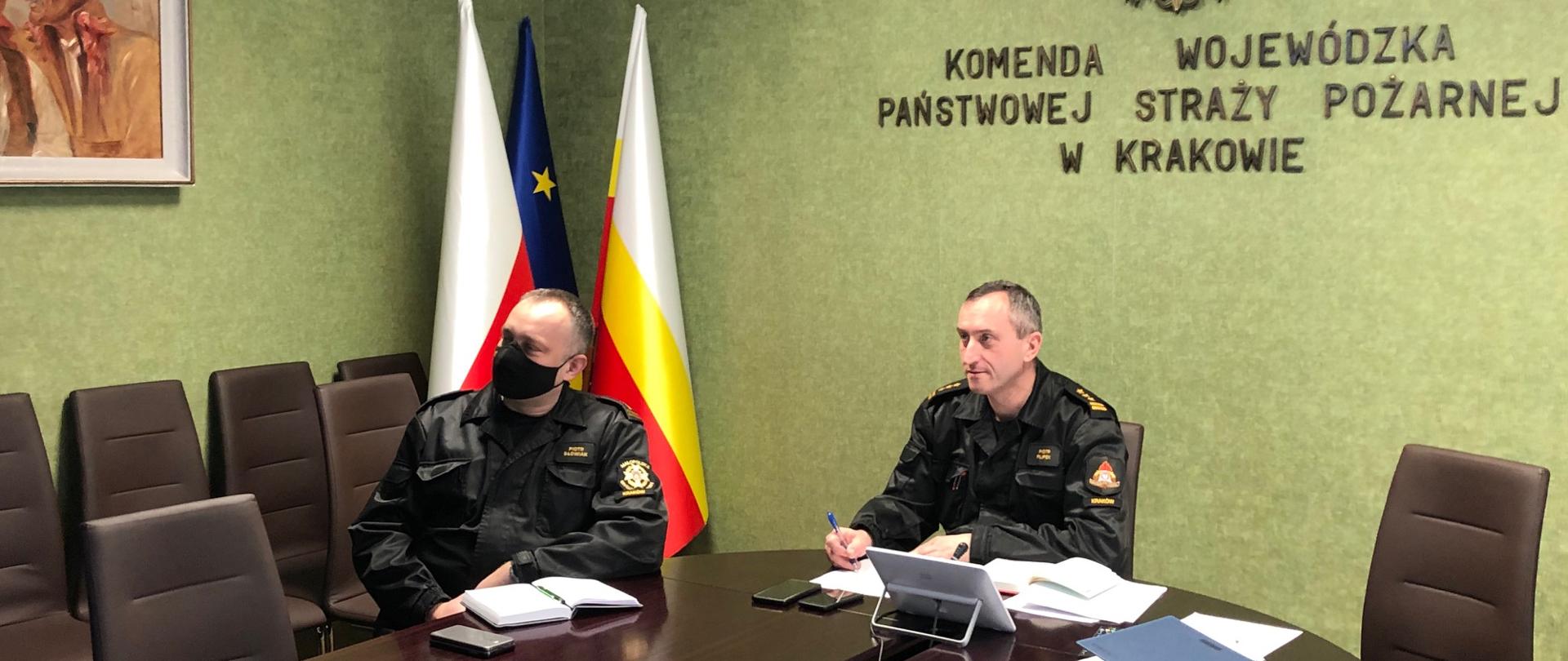 Dwóch mężczyzn w mundurach siedzi przy stole i uczestniczą w wideokonferencji.