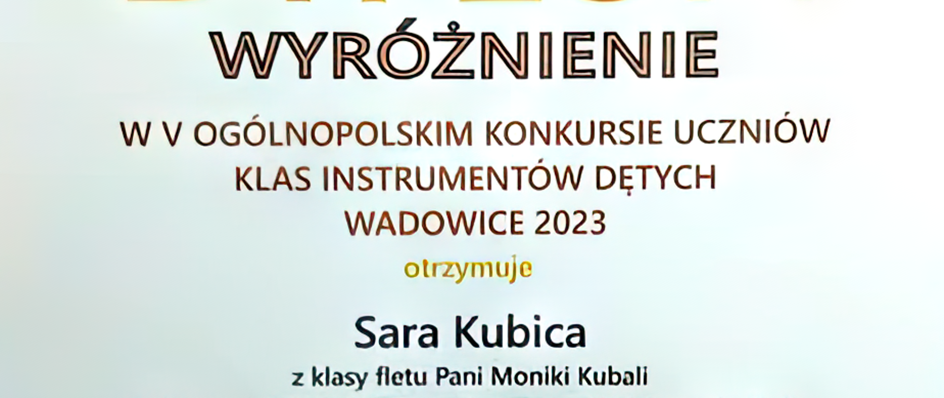 Dyplom na białym tle z motywem trąbki w kolorze żółtym u góry strony oraz napis V Ogólnopolski Konkurs Uczniów Klas Instrumentów Dętych", "Wadowice 2023". Na dyplomie napis "Wyróżnienie w V Ogólnopolskim Konkursie Uczniów Klas Instrumentów Dętych, Wadowice 2023 otrzymuje Sara Kubica z klasy fletu Pani Moniki Kubali, Państwowa Szkoła Muzyczna I st. nr 1 w Kędzierzynie-Koźlu". Na dole strony podpisy jurorów.