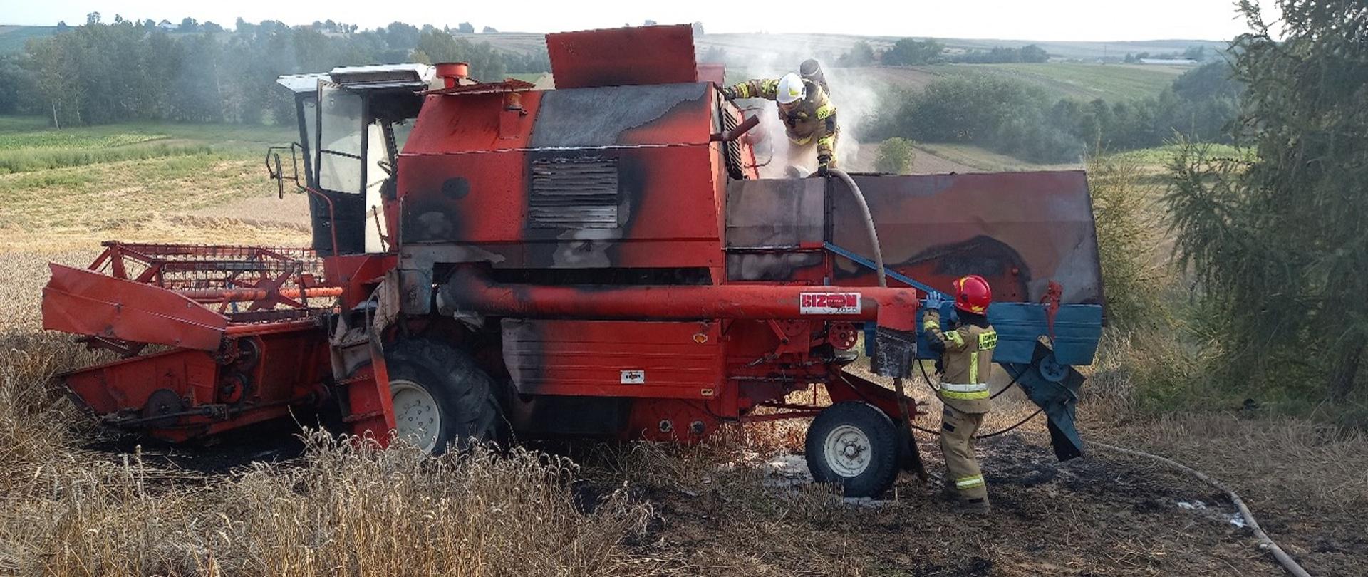 Strażacy dogaszają pożar kombajnu zbożowego podczas zbiorów.